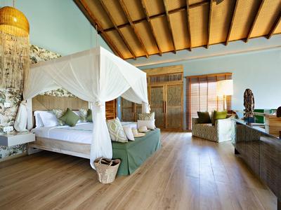 Elegantní hotelový pokoj s baldachýnovou postelí, dřevěnou podlahou a tropickým dekorací.