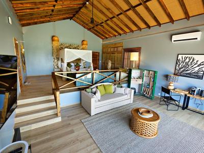 Moderní obývací prostor s bílou pohovkou, ratanovým stolkem a dřevěnou podlahou pod dřevěným stropem.