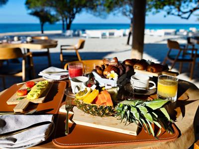 Tropická snídaně podávaná na stole na terase s výhledem na moře.