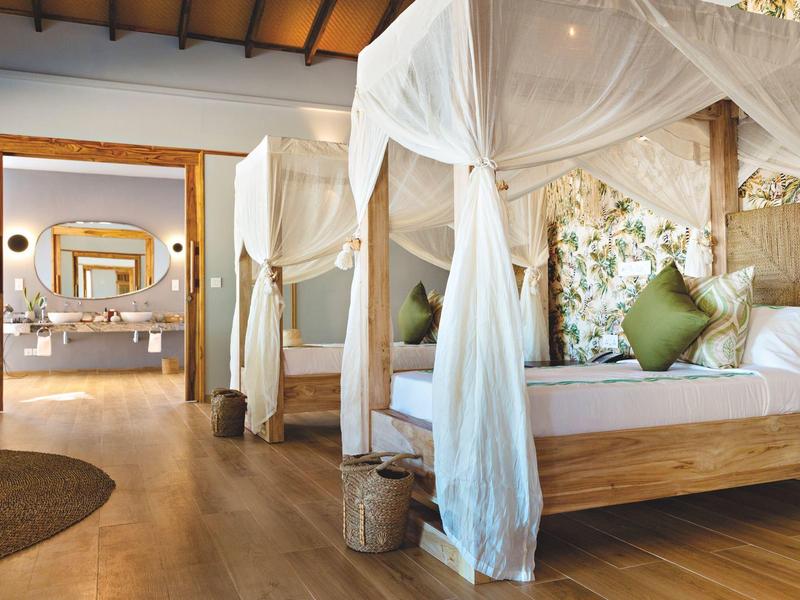 Světlo, útulný hotelový pokoj s postelí s nebesy a dřevěnou podlahou.