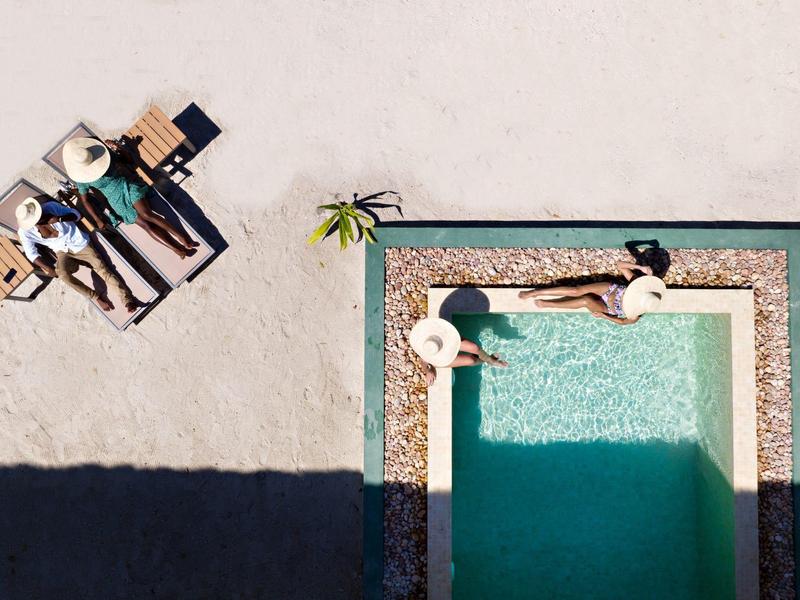 Letecký pohled na bazén s dvěma lidmi relaxujícími u okraje a na pláži.