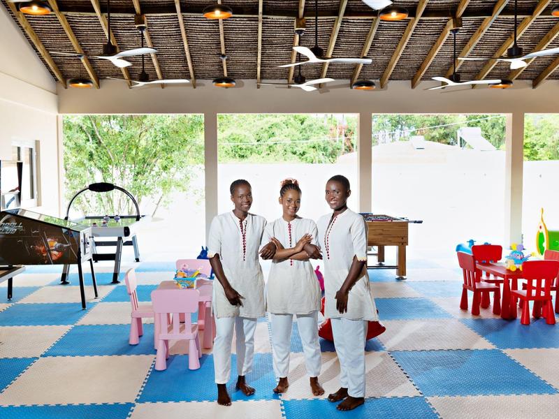 Tři zaměstnanci v uniformách stojí v dětské herně s barevnými hračkami.