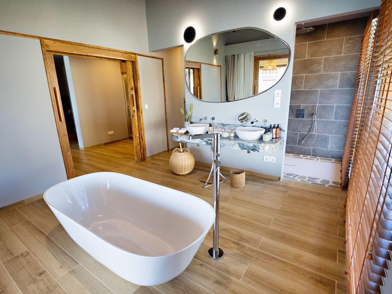 Moderní koupelna s volně stojící bílou vanou a světlou dřevěnou podlahou.