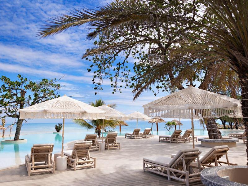 Hotelová terasa s lehátky, slunečníky a výhledem na moře pod modrou oblohou.