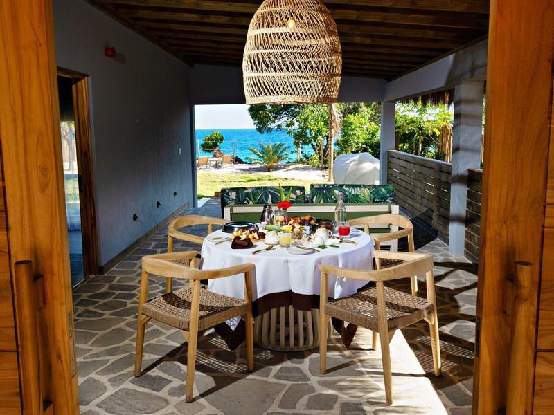 Dřevěná terasa s prostřeným stolem a výhledem na moře pod střešními trámy.