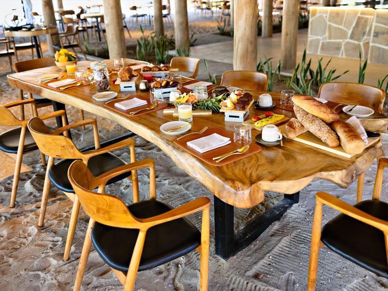 Stůl z přírodního dřeva prostřený s chlebem, nápoji a dřevěnými židlemi.