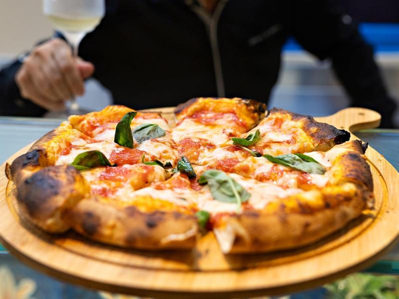 Čerstvě upečená pizza s bazalkou na dřevěném prkénku, podávaná v restauraci.