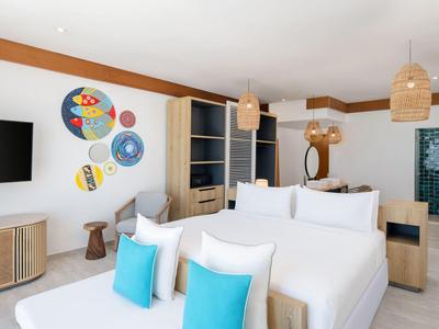 Modern hotel room with two large beds, blue pillows, and wall decorations.