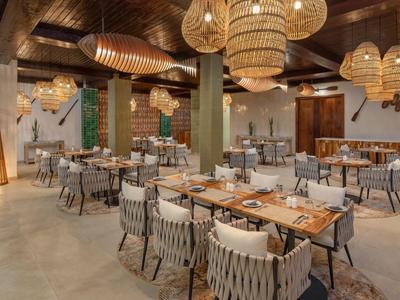 Modern hotel restaurant with wooden ceilings, round lamps, and gray chairs at wooden tables.