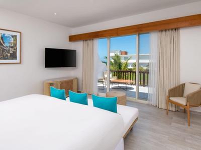 Modern hotel room with large bed, TV, and balcony overlooking the sea.