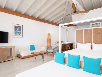 Modern hotel room with white canopy bed and blue accent pillows in bright space.
