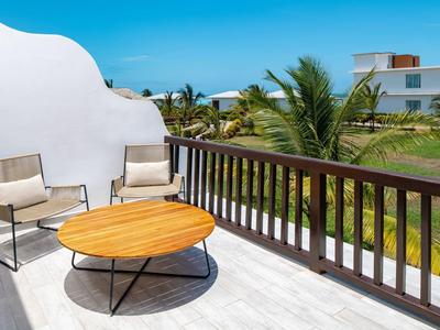Balcony with two chairs and round wooden table overlooking palm trees and modern building.