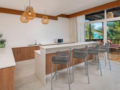 Modern kitchen with breakfast bar and stools, large sliding glass door to balcony with palm view.