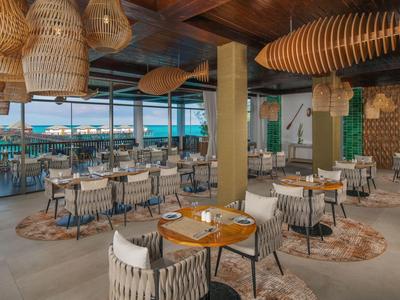 Modern restaurant with wooden accents, wicker lights, and sea view.