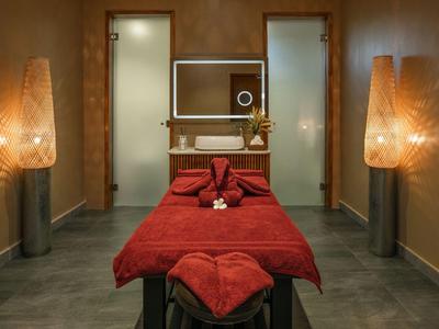 Cozy massage room with red bed and warm-lit walls for relaxation.