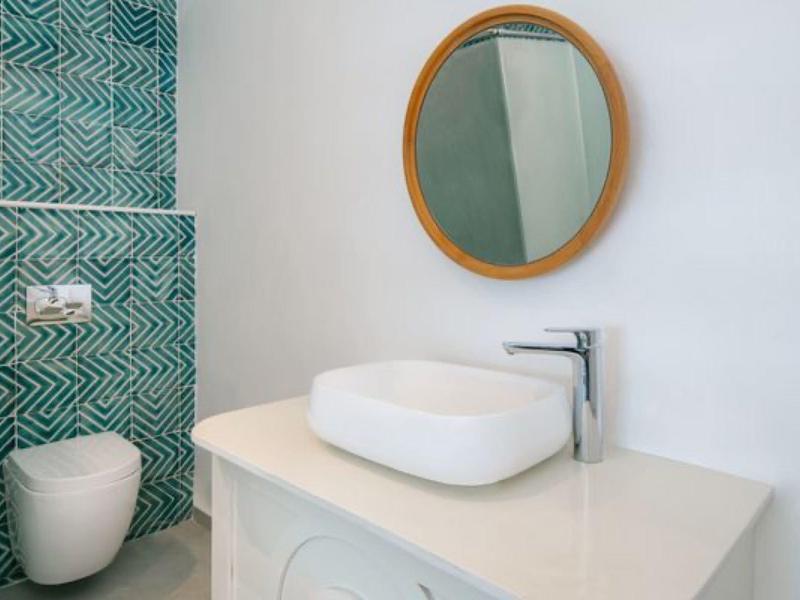 Modern bathroom with oval mirror, white sink, and green-blue patterned wall.