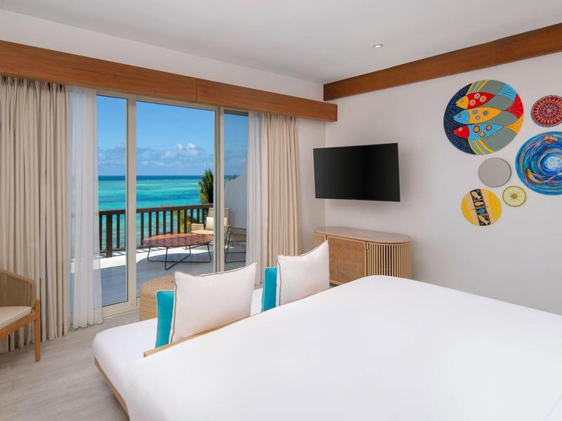 Hotel room with white bed, colorful wall decor, and balcony overlooking the sea