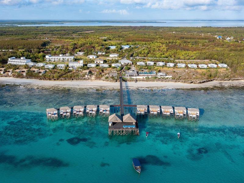 Overview of a resort with beach and overwater bungalows in turquoise blue sea.
