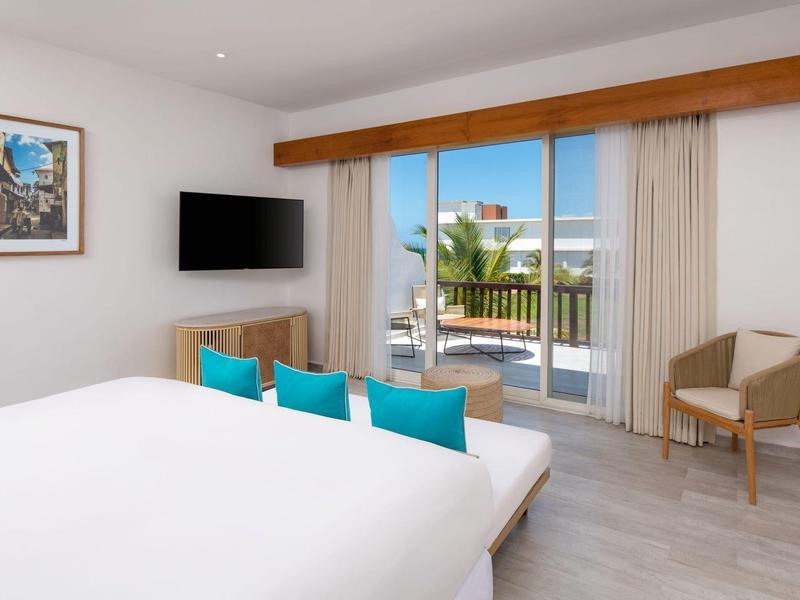 Modern hotel room with large bed, TV, and balcony overlooking the sea.