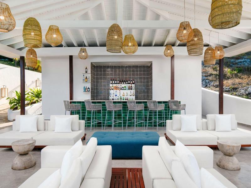 Modern outdoor lounge with white sofas and green tiled bar under wooden lights.