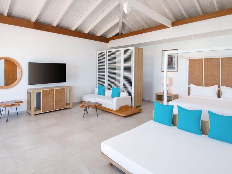 Modern hotel room with white furnishings, wood accents, and blue cushions.