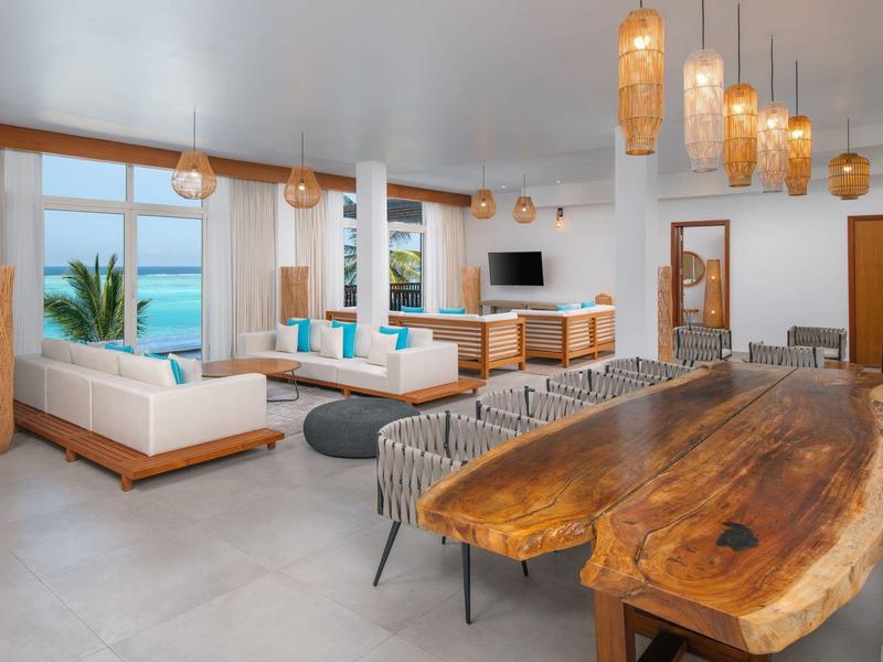 Spacious modern living and dining area with wooden table, white sofas, and sea view.