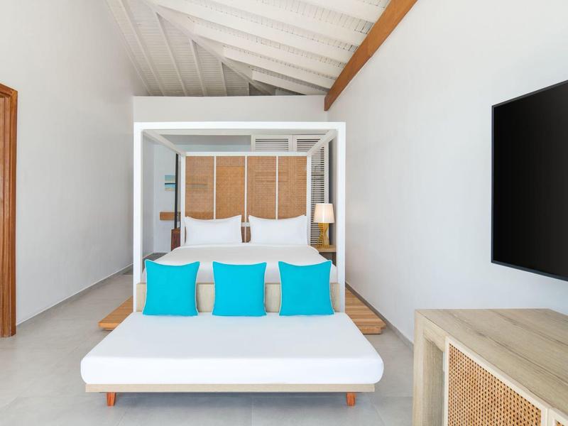 Modern hotel room with canopy bed, turquoise pillows, and wall-mounted TV.