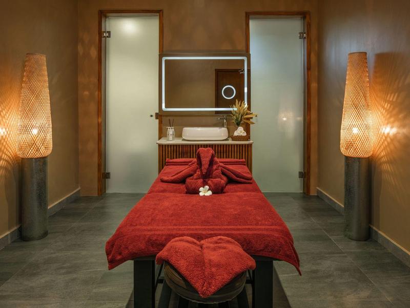 Cozy massage room with red bed and warm-lit walls for relaxation.