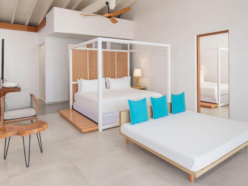 Modern hotel room with canopy bed, chair, mirror, and minimal color palette.