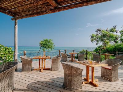 Offene Terrasse mit Holzstühlen und Tischen, Blick auf Meer und klaren Himmel.