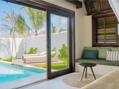 Helles Wohnzimmer mit gemütlicher Couch, kleinem Tisch, Blick auf Pool und Garten durch große Schiebetür