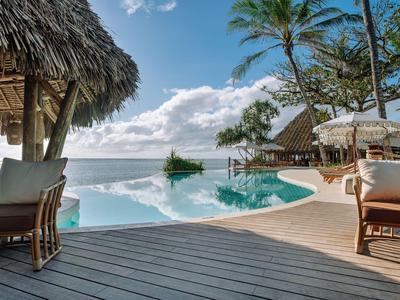 Luxurious pool area with wooden deck, palm trees, and sea view under a blue sky.