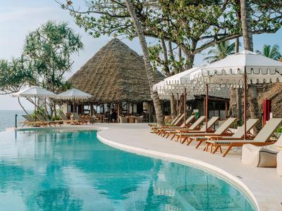 Una piscina con tumbonas y sombrillas junto a árboles y agua de fondo.