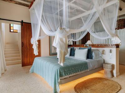 Helles Hotelzimmer mit Himmelbett, weißem Netz und blauem Bettüberwurf.