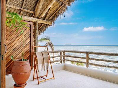 Balkon mit Holzgeländer, Stuhl und Terrakottakanne, mit Blick auf Meer und blauen Himmel.
