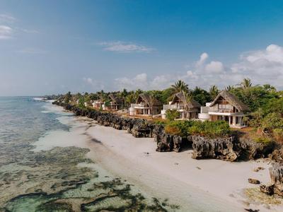 Strand mit weißen Sand, Felsen und Bungalows am Küstenrand bei blauem Himmel