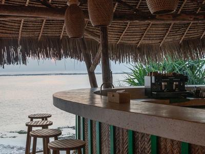 Bar rústico con taburetes de madera y techo de paja en la playa con vista al mar.