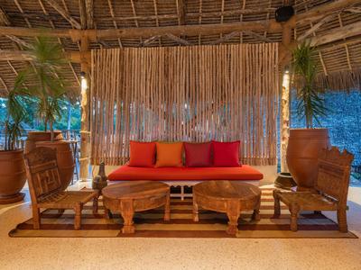Einladender Sitzbereich mit roten Kissen, Holzmöbeln und Pflanzen unter einem Strohdach.