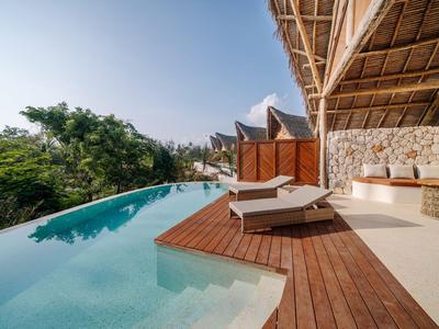 Infinity-Pool mit Liegestühlen auf Holzdeck und tropischer Aussicht bei klarem Himmel.