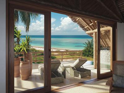 Vista a través de puertas de vidrio hacia terraza con tumbonas y océano al fondo