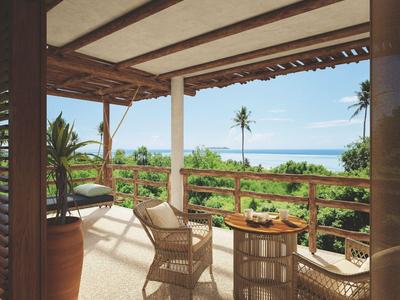 Veranda abierta con sillas de mimbre, mesa y vista a la vegetación tropical y el océano.