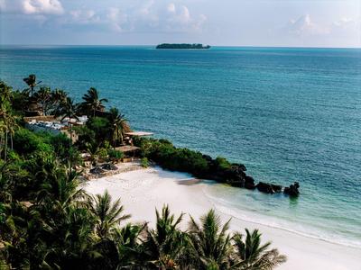 Kleine tropische Bucht mit weißem Sand, Palmen und einer Insel am Horizont.