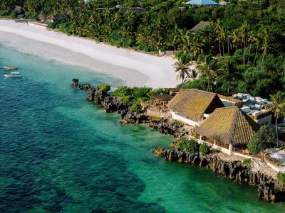 Un complejo tropical en la playa con playas de arena blanca, agua turquesa clara y chozas con techos de paja.