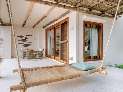 Moderner Balkon mit Hängematte, Sitzbereich und Holzrahmenfenstern unter einem Strohüberdach.