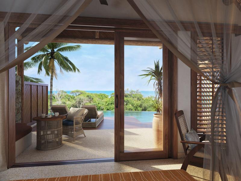 Blick von einem Schlafzimmer auf eine Terrasse mit Pool, Lounge-Möbeln und Palmen am Meer.