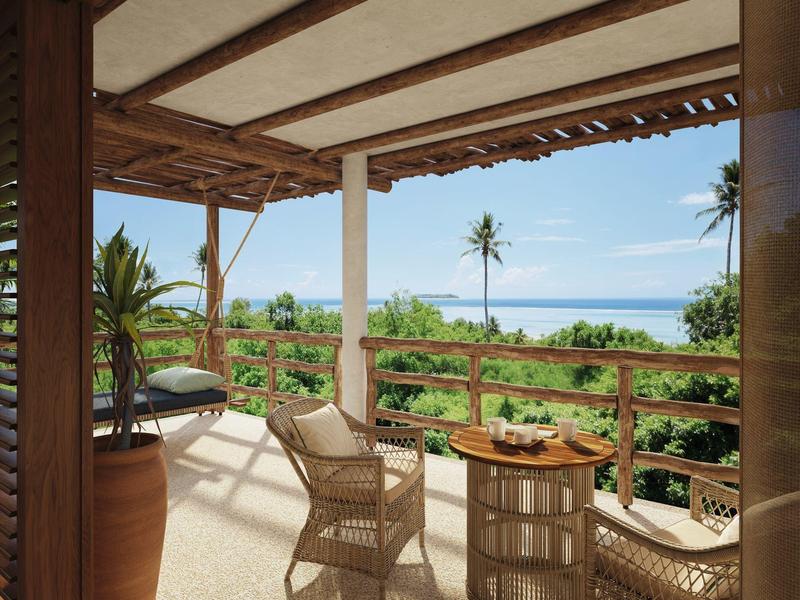 Terrassenblick mit Bambusmöbeln, grünem Garten und weiter Meersicht unter blauem Himmel.