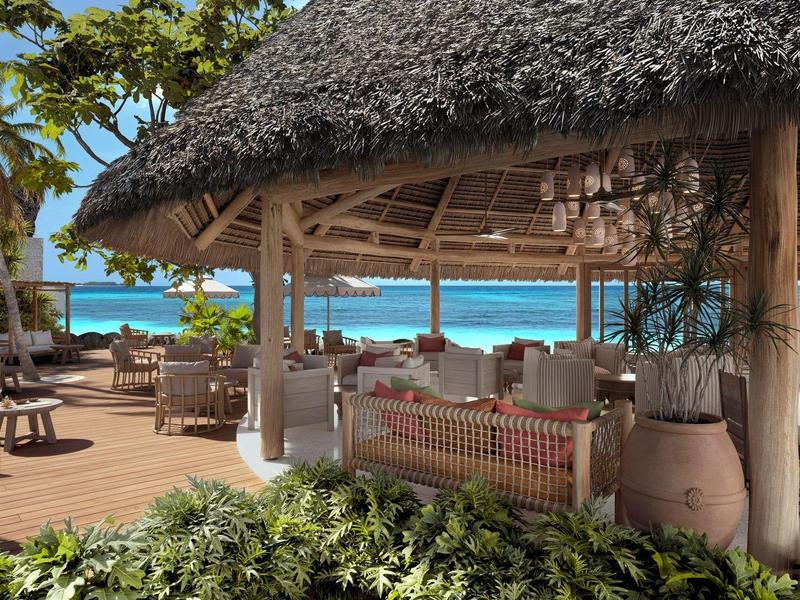 Strandrestaurant mit Strohdach, Holzstühlen, Tischen und Blick auf tropisches blaues Meer.