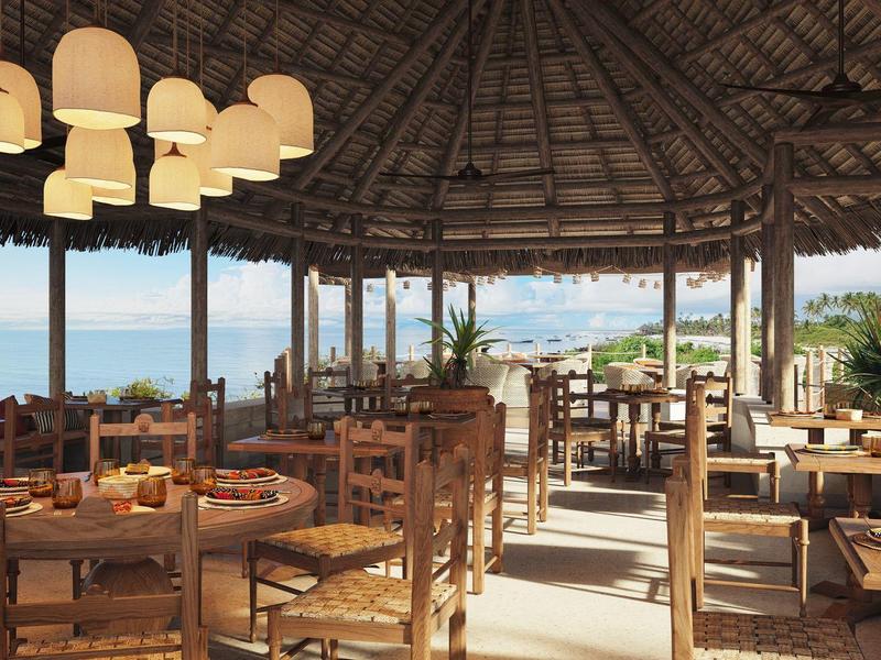 Offener Restaurantbereich mit Holzmöbeln, Strohdach und Meerblick im Hintergrund.