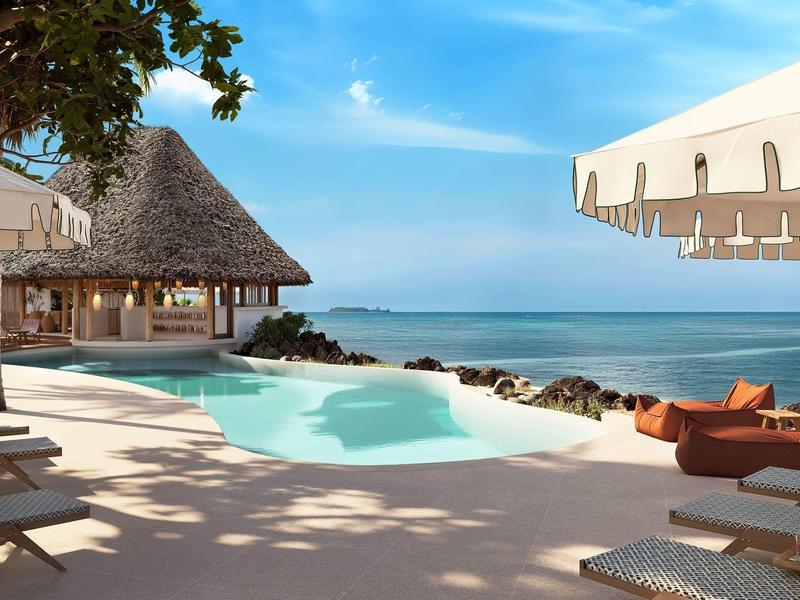 Luxuriöser Poolbereich mit Liegestühlen, Sonnenschirmen und Blick auf das blaue Meer unter klarem Himmel.