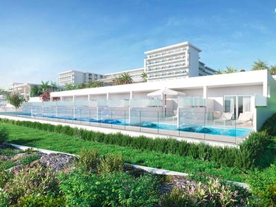 Nowoczesny hotel z tarasem przy basenie i przyległym zielonym terenem pod niebieskim niebem.